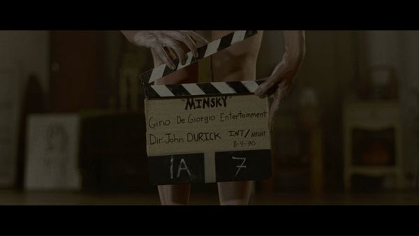 Still from Immortality, featuring hands holding a film clapper in front of legs, just below the knee